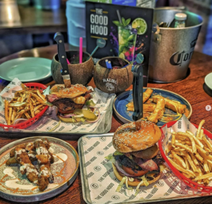 Good Hood table of food featuring Burgers, chicken wings, fries and cocktails